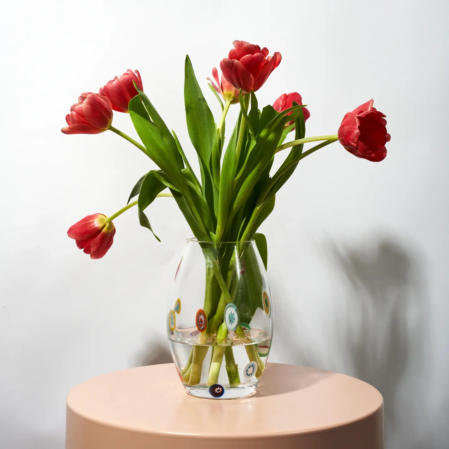glass vase holding red roses, sitting on side table