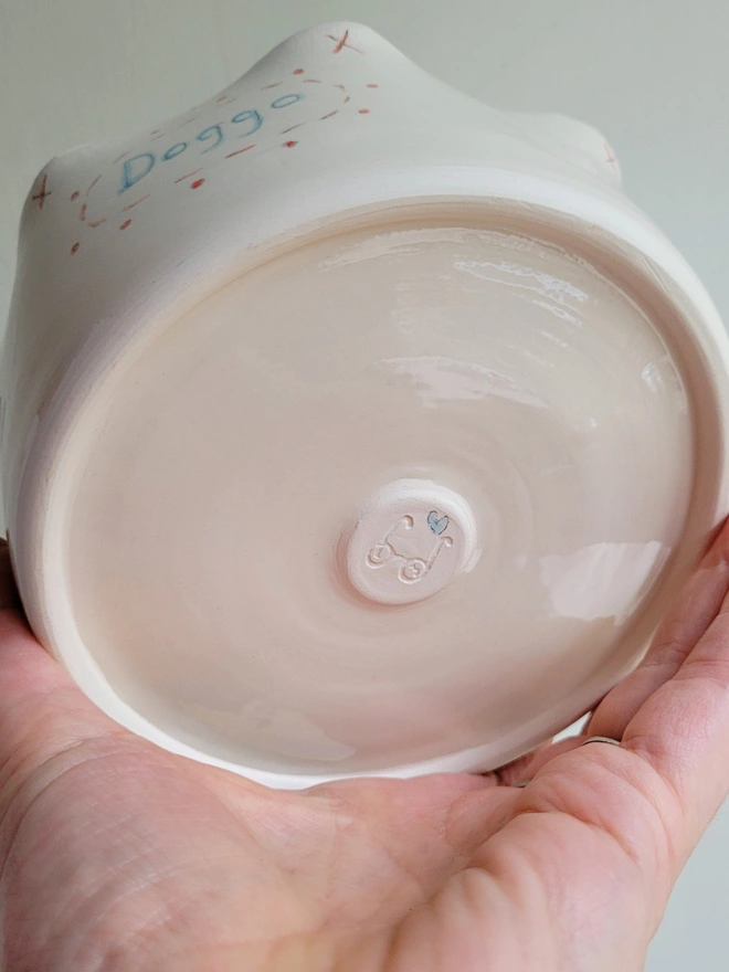 a ceramic dog bowl held in a hand to show the underside with a small painted blue heart