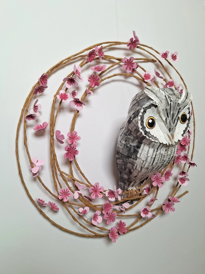 side view of woodland wall art, depicting a white faced owl perched on a pink wreath of handmade paper flowers 