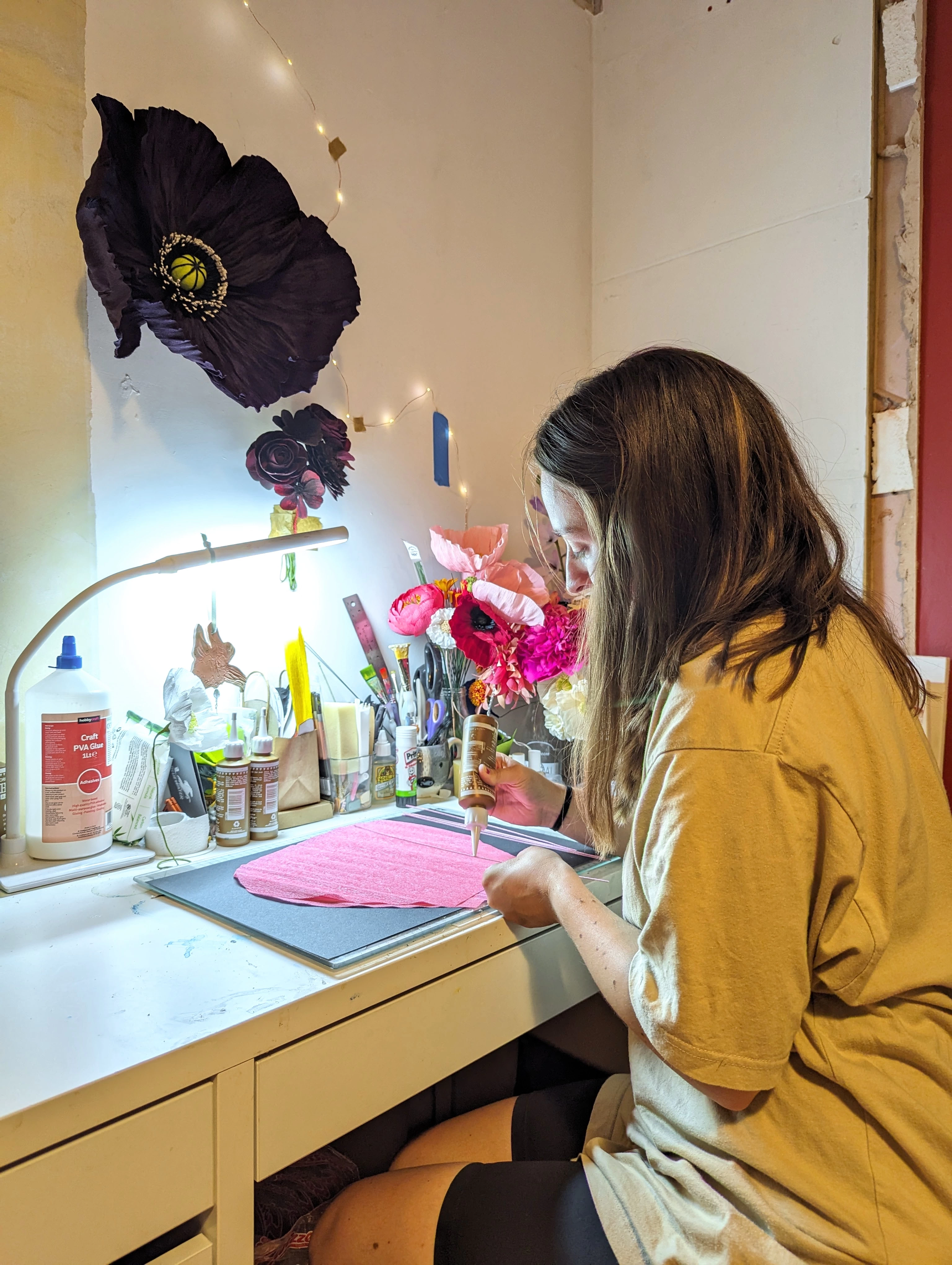 Photograph shows artist sitting at her desk making paper flowers