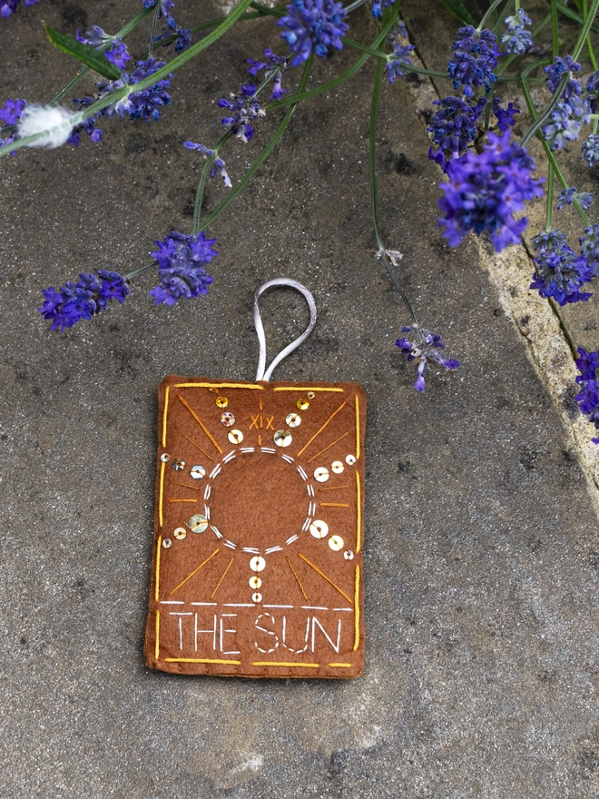 A handcrafted felt ornament with sequins and embroidery depicting "The Sun" tarot card