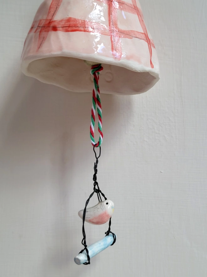 pink ceramic budgie on a swing hanging from a pottery bell with pink and red gingham check