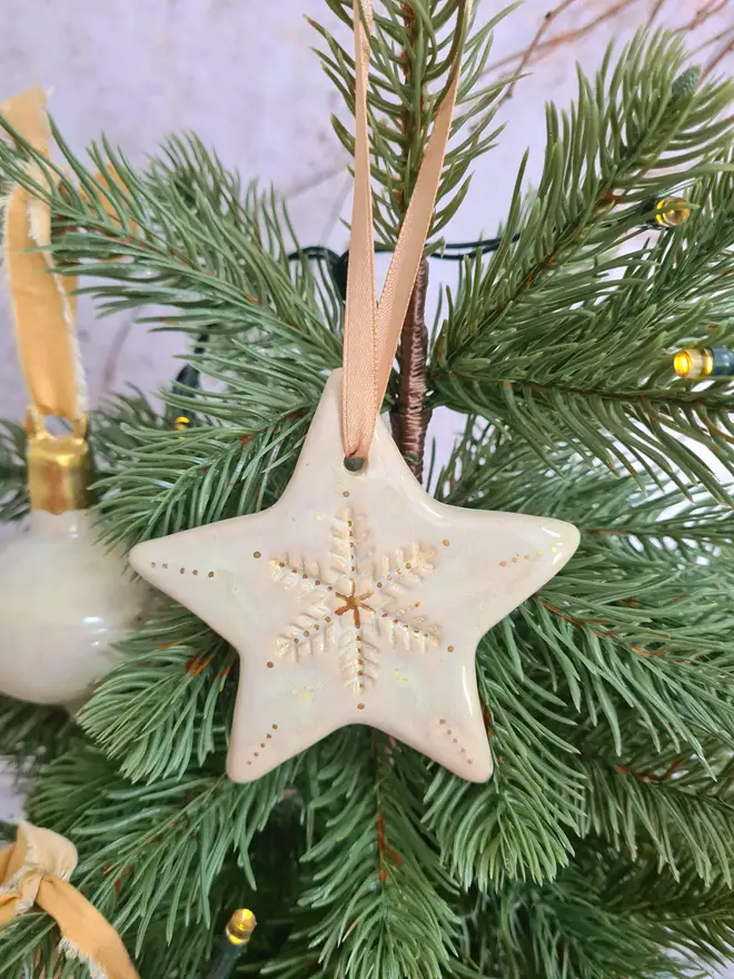 Star Christmas decorations, ceramic decorations, dream catcher, christmas star, pottery, Jenny Hopps Pottery, J.H Pottery, J.Hopps Pottery, Clay star, gift, christmas tree, blue with white and cream with gold details, on a light gold ribbon, photographed on a branch with Christmas lights