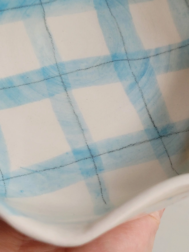 the inside of a fluted rimmed ceramic dog bowl with a blue gingham check inside