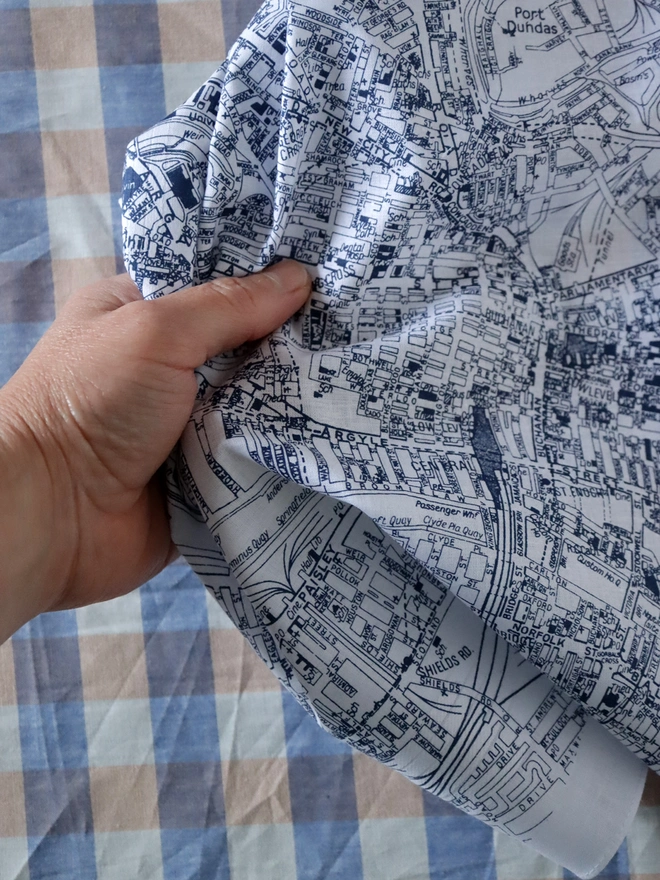 Glasgow handkerchief held by a white hand in front of a gingham, tablecloth