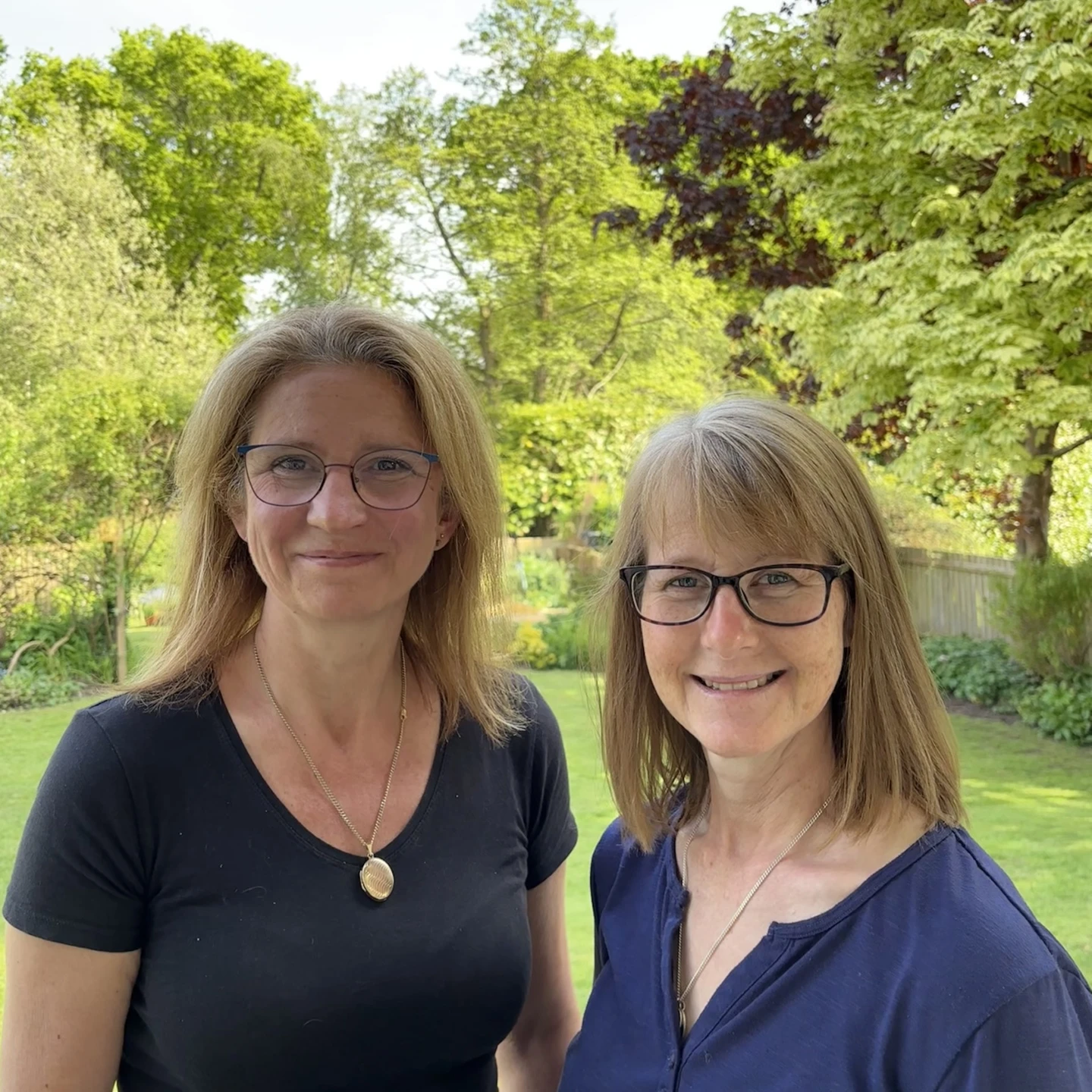 2 ladies standing next to each other with trees in the background