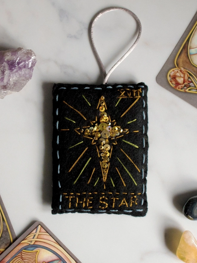 A handcrafted felt ornament with sequins and embroidery depicting "The Star" tarot card. 