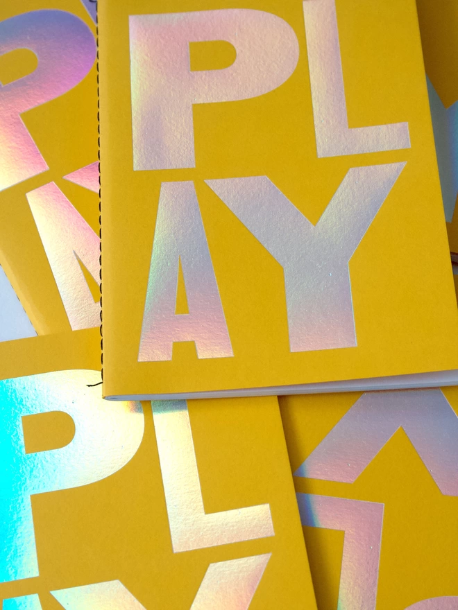 A pile of yellow notebooks with the word 'play' on the front