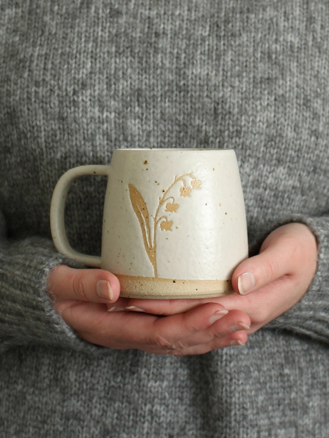 Hands holding lily of the valley mug