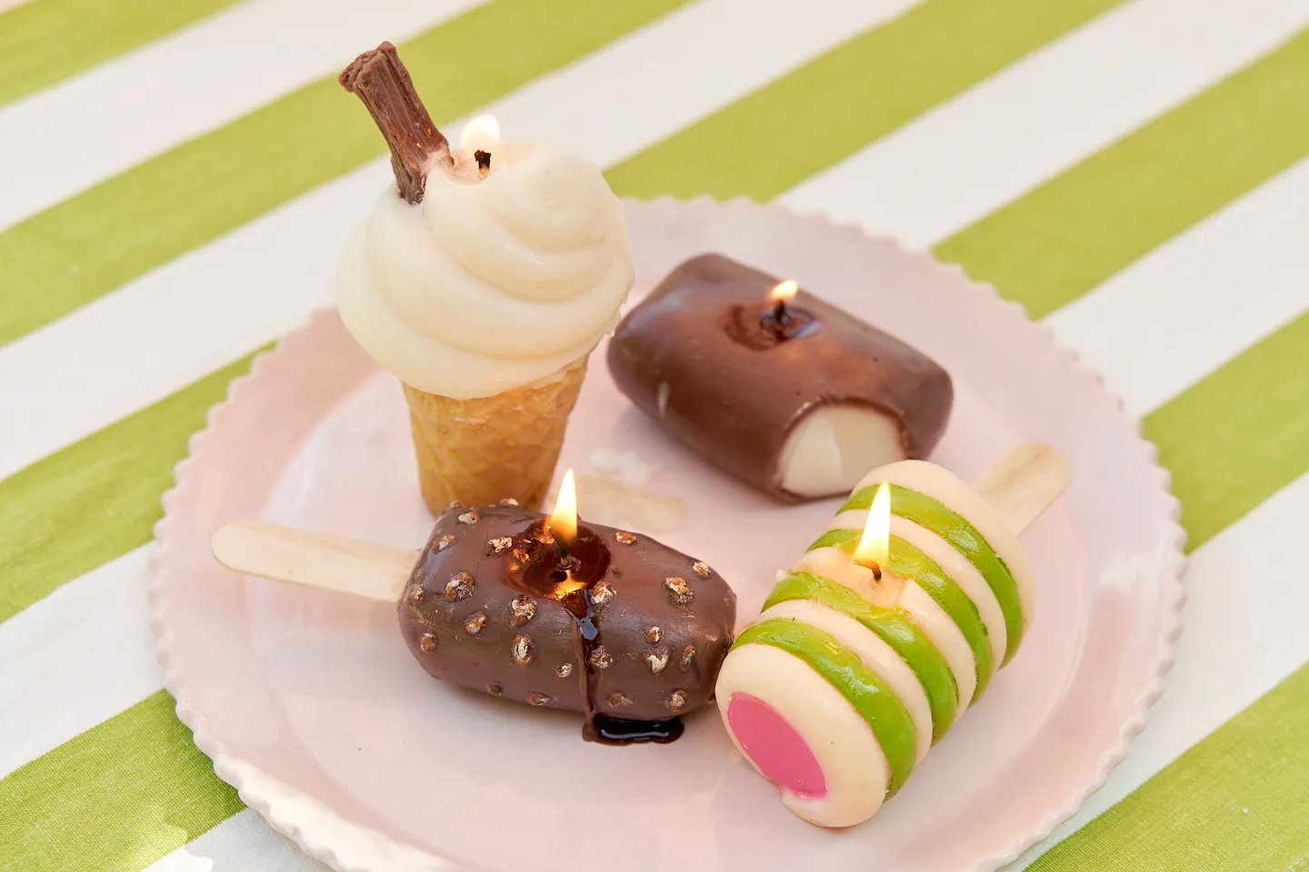 Ice cream fake food shaped candles on a pink plate and green striped tablecloth