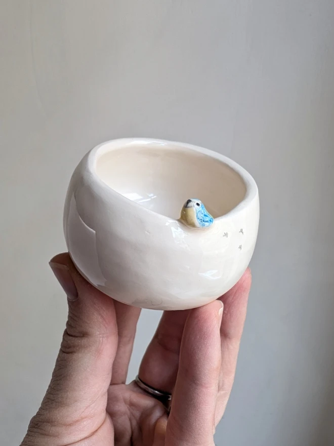 blue tit tealight in white earthenware ceramic with a tiny pottery bluetit bird and birdprints held in a hand