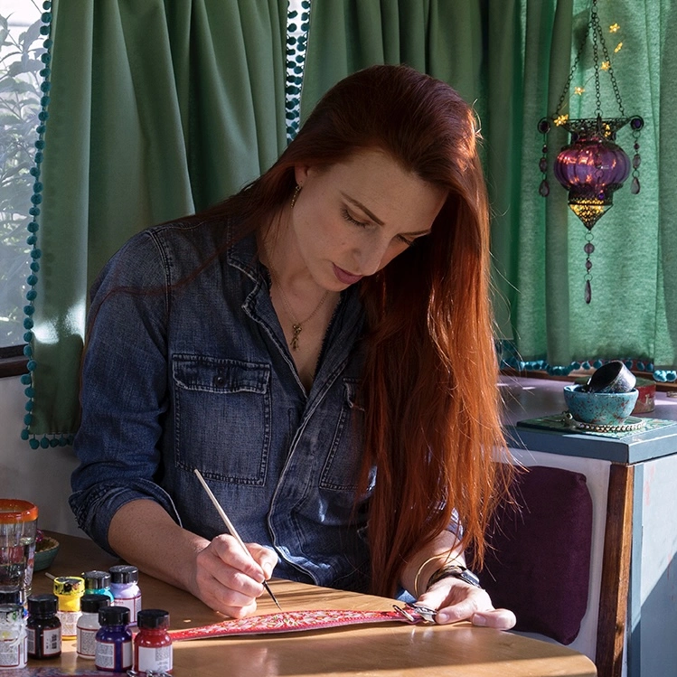 Last Night in Limehouse founder and maker sits at a desk hand painting a leather sighthound collar with an original colourful boho design