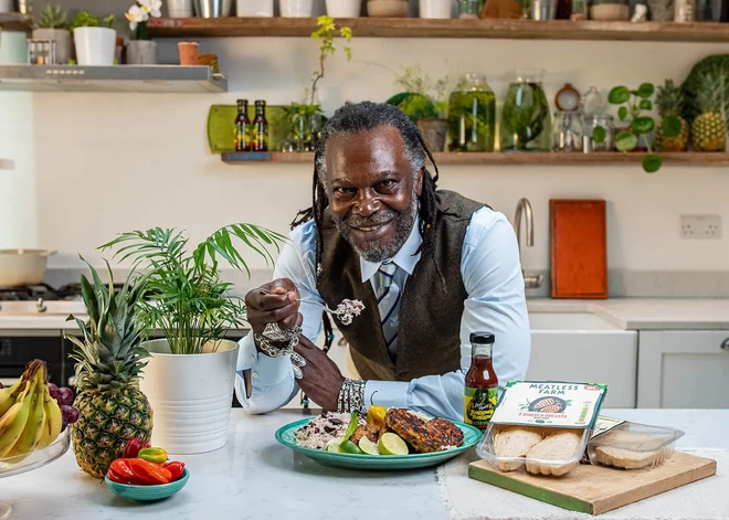 Levi Roots, founder of Reggae Reggae Sauce, smiling at the camera in a kitchen.