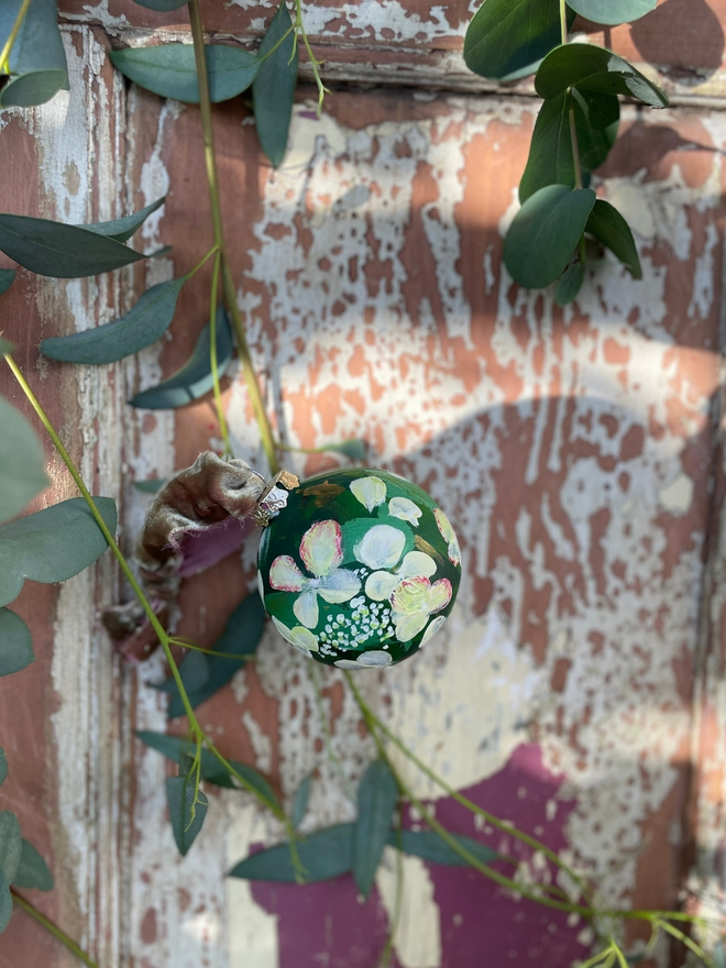 hand painted ceramic Christmas bauble deep green background adorned with white hydrangeas.