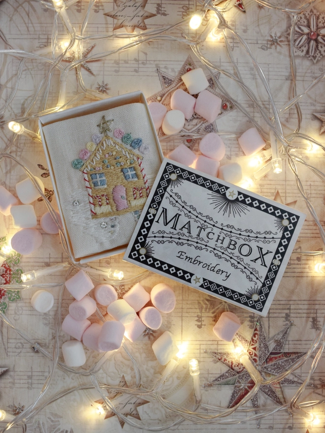 A delicious embroidered gingerbread house covered in sweets.  Displayed in its matchbox, surrounded by mini marshmallows and fairy lights.