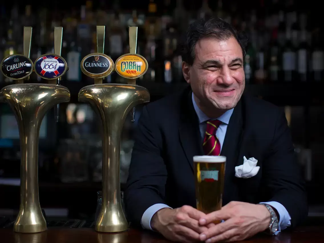 Lord Karan Bilimoria CBE, DL, founder of Cobra Beer, smiling into the distance while holding a beer.
