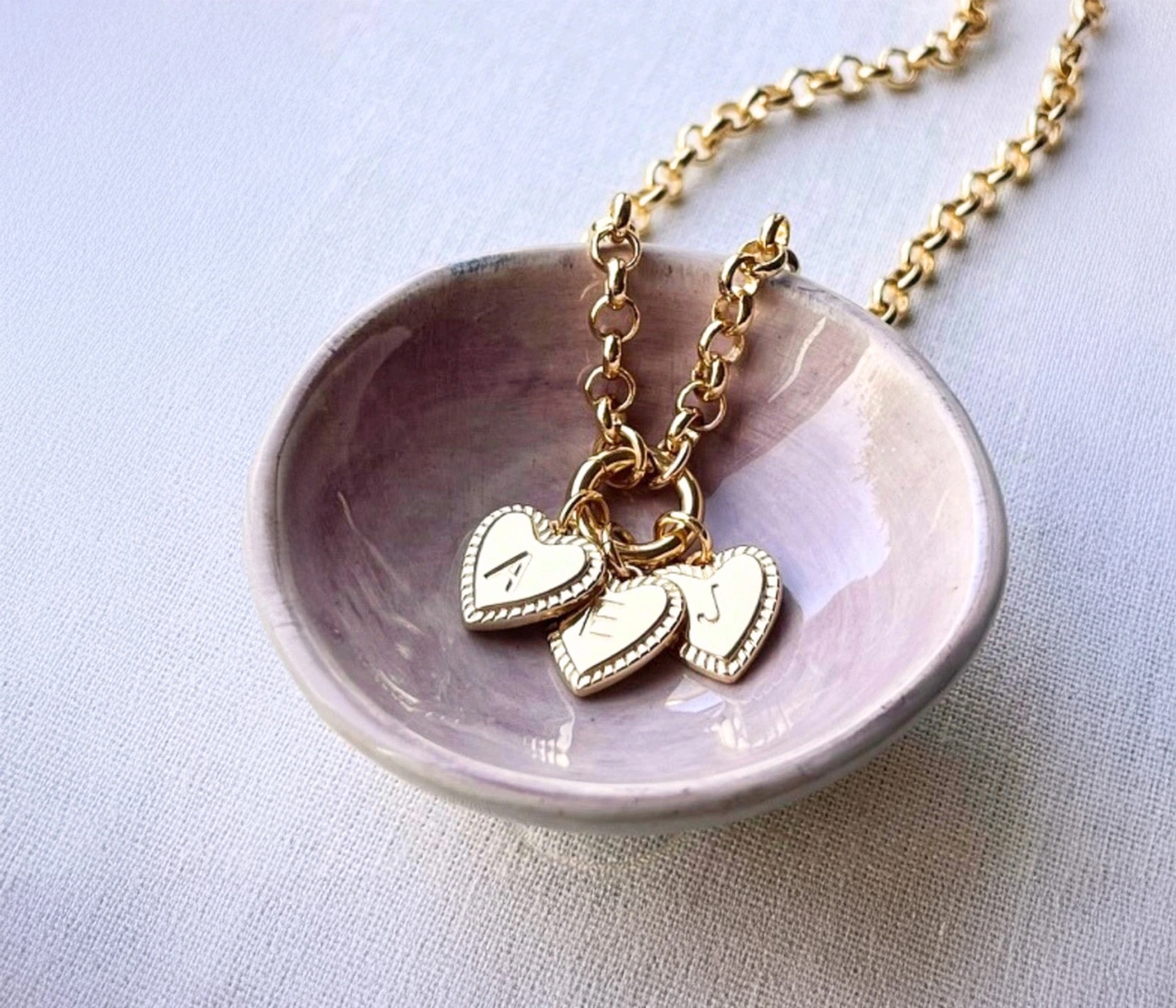 Family charm necklace. A gold charm necklace with three initial heart charms on a belcher chain.