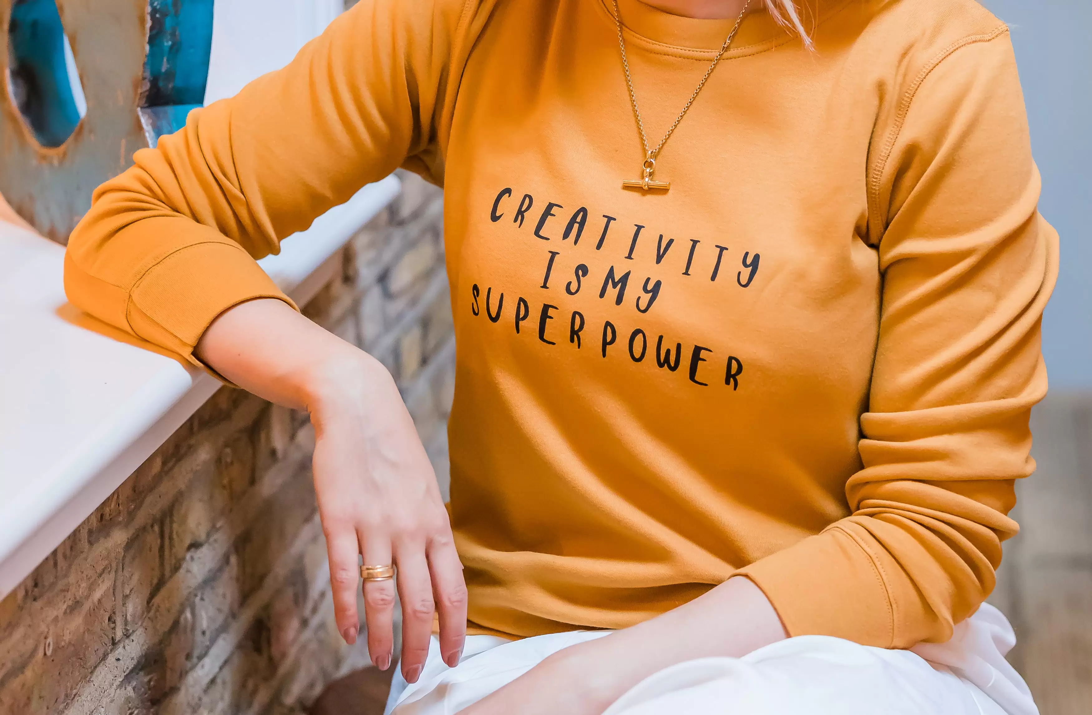 Woman sat wearing a mustard jumper with creativity is my superpower written on it 