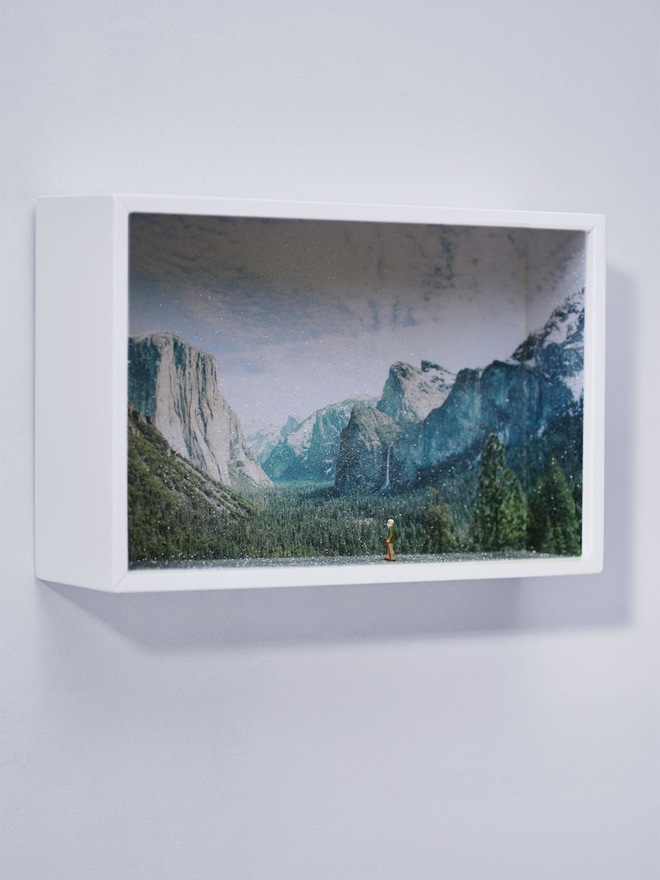 Miniature scene in an artbox showing a tiny man hiking towards a sparkling mountainous backdrop. 