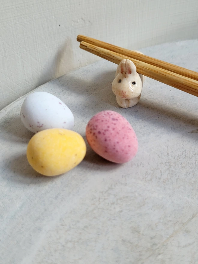 a little beige bunny ceramic chop sticks holder with chop stix resting on top and Easter mini chocolate eggs in the foreground