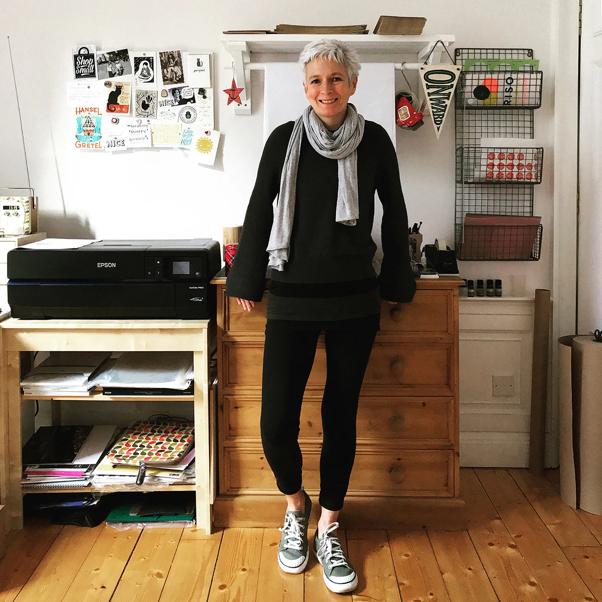 woman with white hair dressed in black clothes and a grey scarf in Edinburgh art studio with wooden floors and art studio equipment