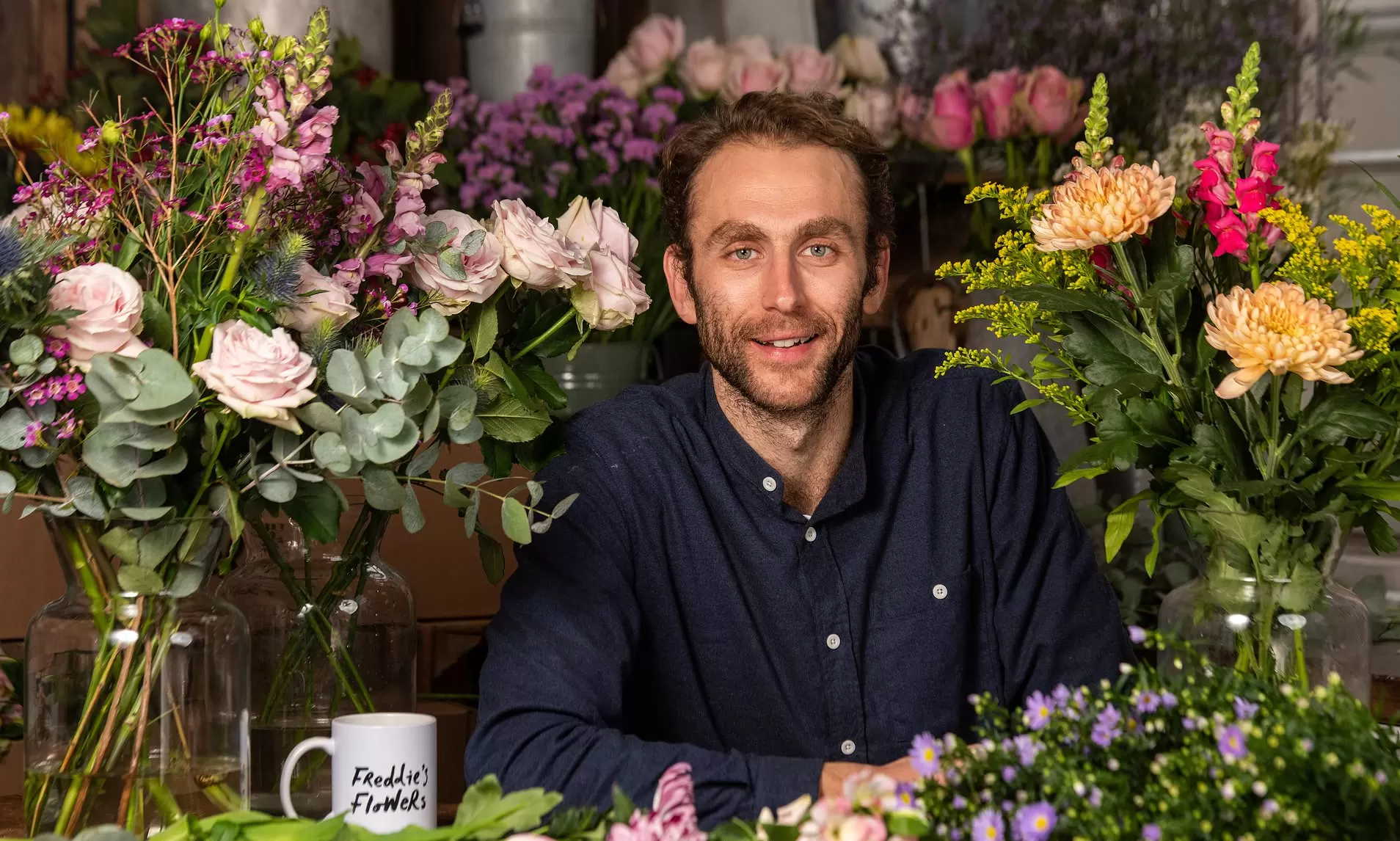 Freddie Garland, founder of Freddie's Flowers, sat surrounded by flowers smiling at the camera.