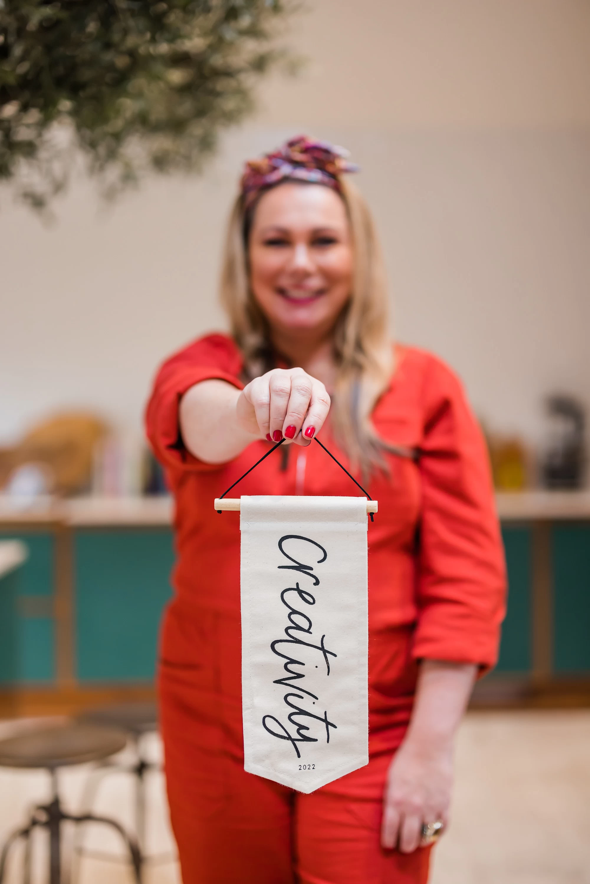 Holly Tucker wearing an orange jumpsuit holding a white pennant with creativity written on it 