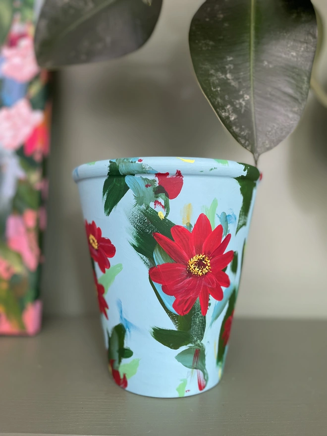 Hand painted pale teal plant pot with vibrant red zinnia flowers 