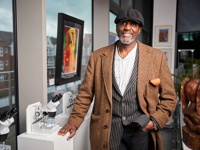 Willard Wigan, creator of the world's smallest sculptures, smiling at the camera, wearing a brown coat and a baker boy hat.