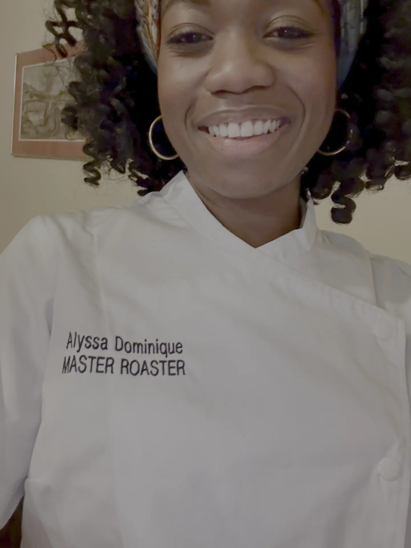 A black woman with curly black hair is shown smiling, wearing a chef jacket that says Alyssa Dominique Master Roaster