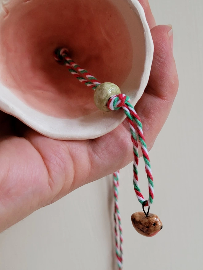 close up of the inside of a pink pottery bell with a ceramic green bead and tiny robin bird bead all held in a hand