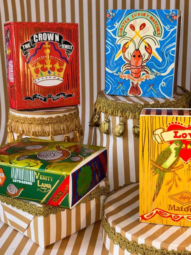 The Crown Jewels Matchbox, a red matchbox with a crown design sitting on a decorated surface accompanied by other accessories. 