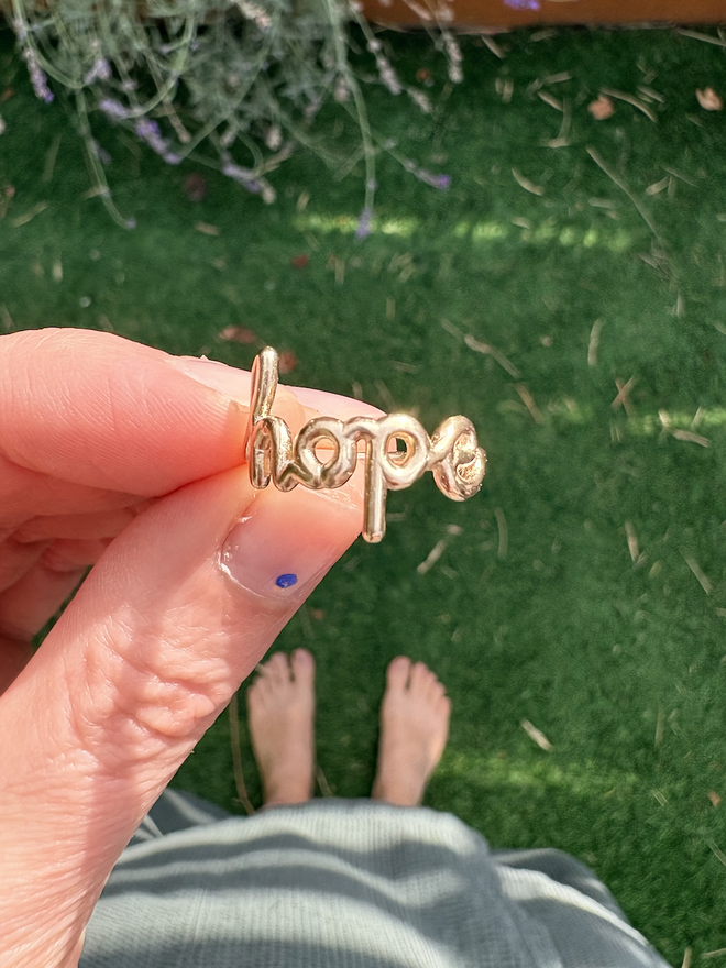 Ring being held that says 'Hope' within it, in 9ct yellow gold