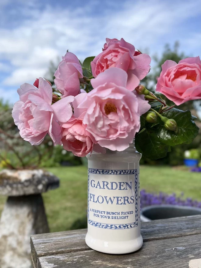 A tall handmade ceramic vase/jar with a blue decoration is filled with garden roses.