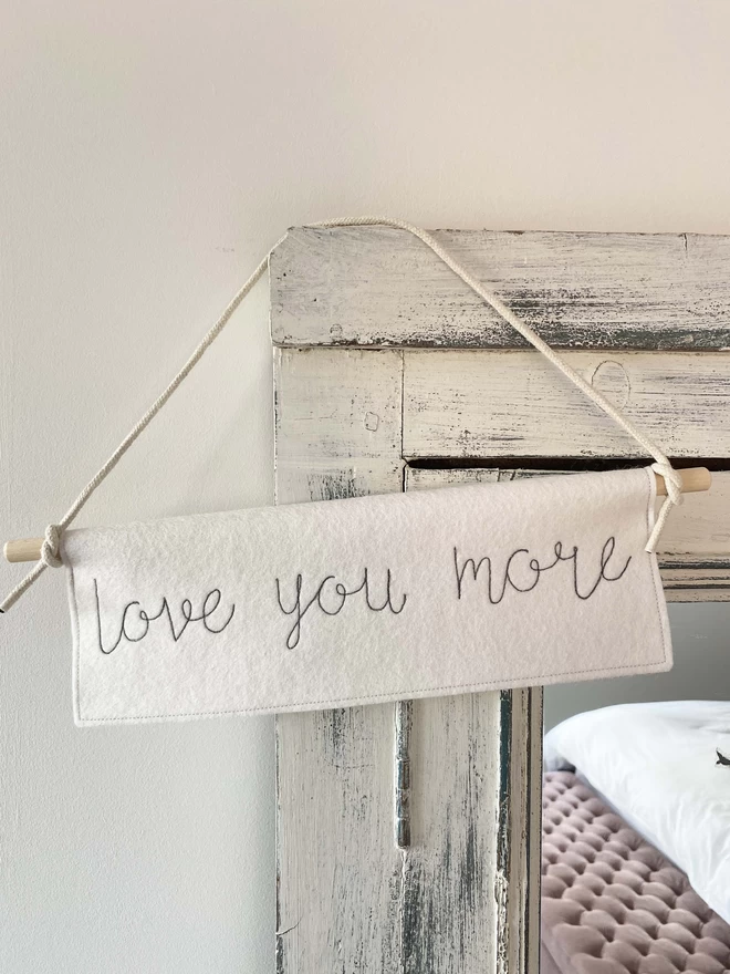 Love You More Felt Embroidered Banner hanging on mirror