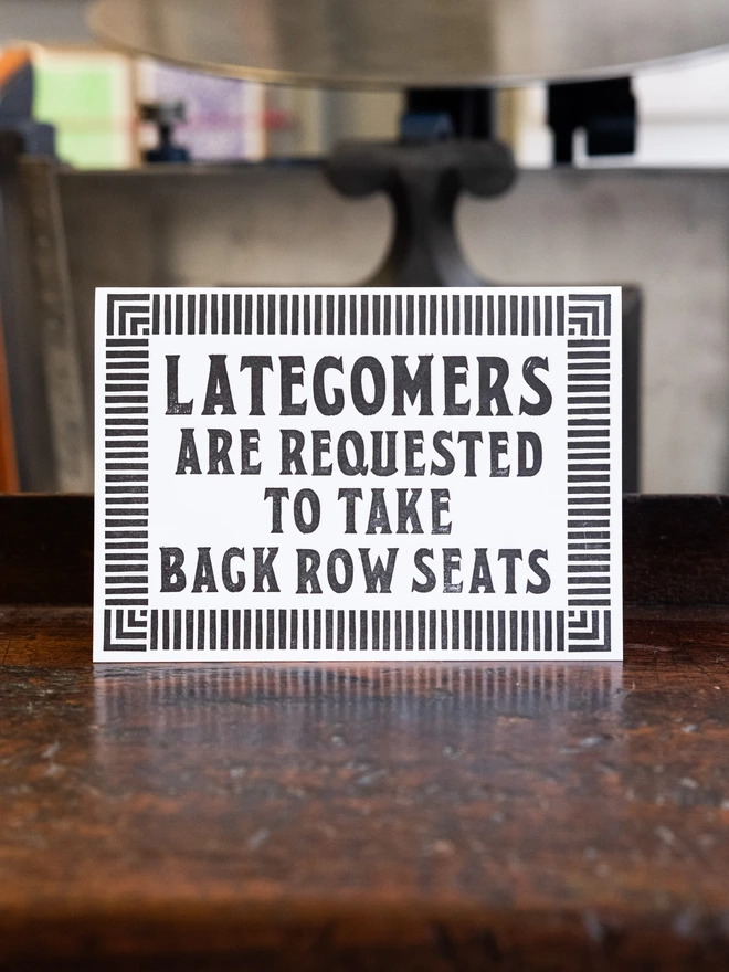 Letterpress card with text design "Latecomers are requested to take back row seats," Surrounded by art deco style border of parallel lines. 