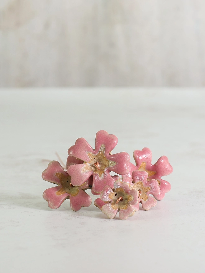 pink ceramic primrose flowers sit on a white background, the flower heads facing front