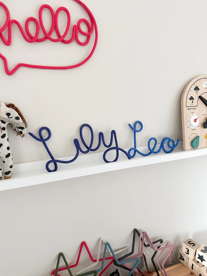 Personalised Baby and Kids Wall and Door Name Sign 'Lily' and 'Leo' on a shelf in a playroom with other kids room decorations and baby nursery toys and signs. 