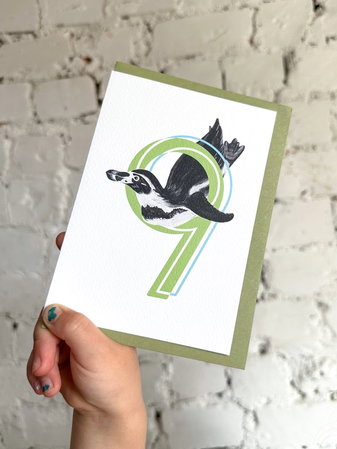 white card with a big green number 9 and a penguin illustration and a green envelope