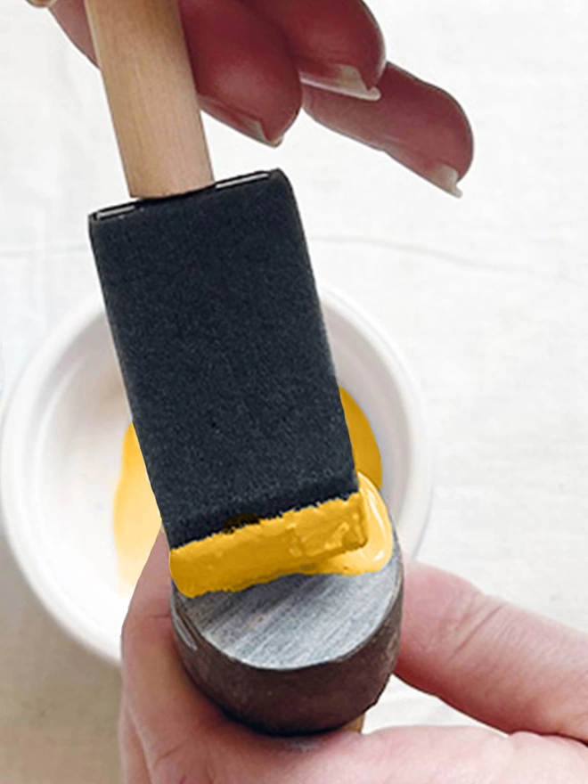 Detail of tow hands holding a small circle wooden block and applying yellow ink with a foam brush