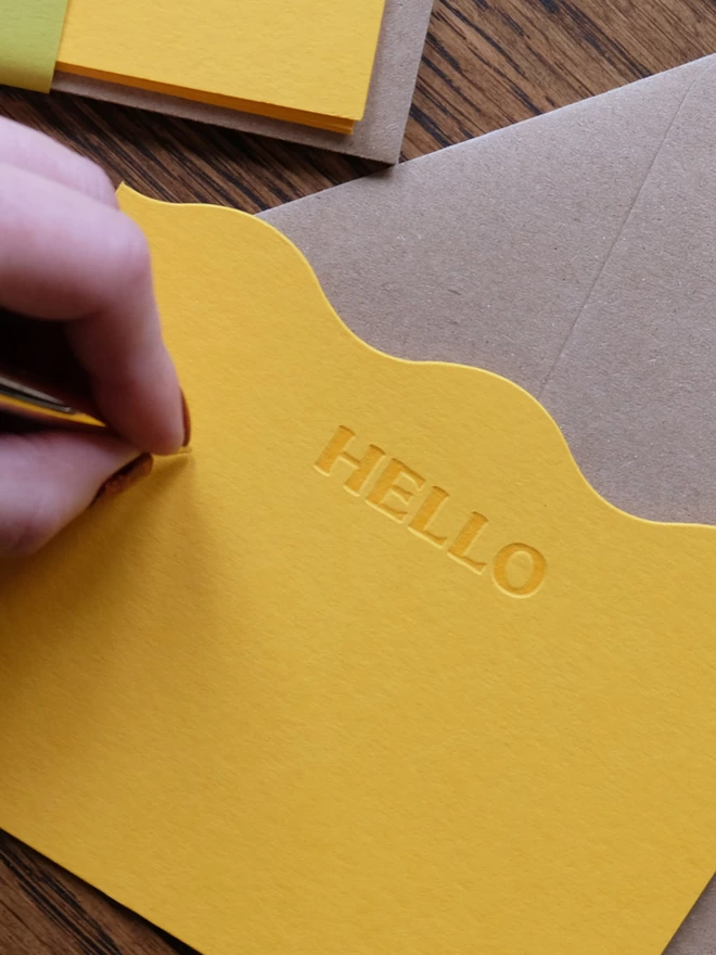 Ladies hand writing on yellow 'Hello' notecard.