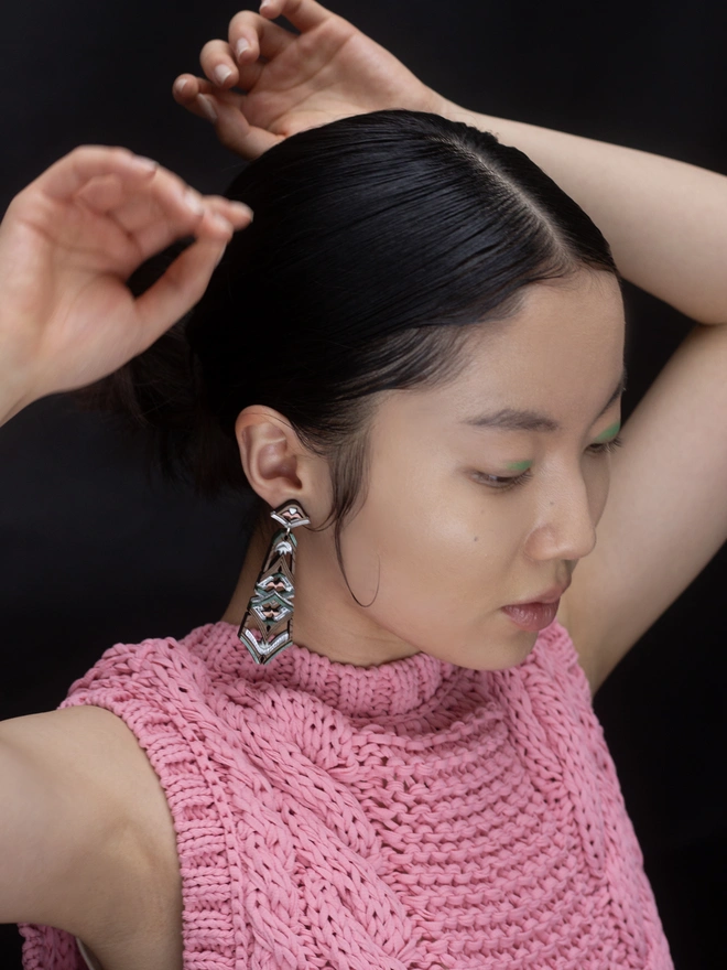laser cut earrings on model with hards above head in front of a black background