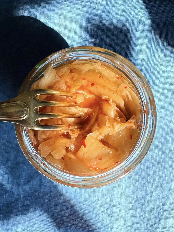 Ferment Intro Journey (Set Of 5), a jar of ferment sitting on a blue surface. It is accompanied by a fork. 