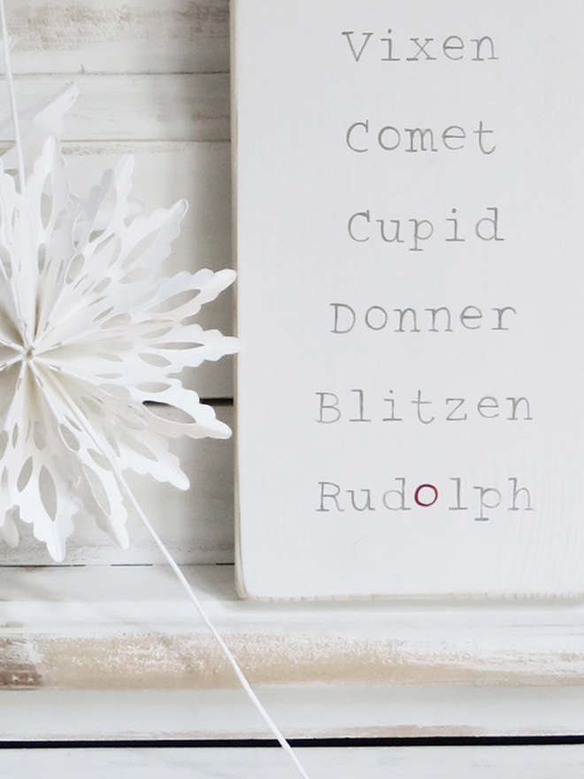white painted wooden sign with reindeer names strung with wire and decorated with ribbon