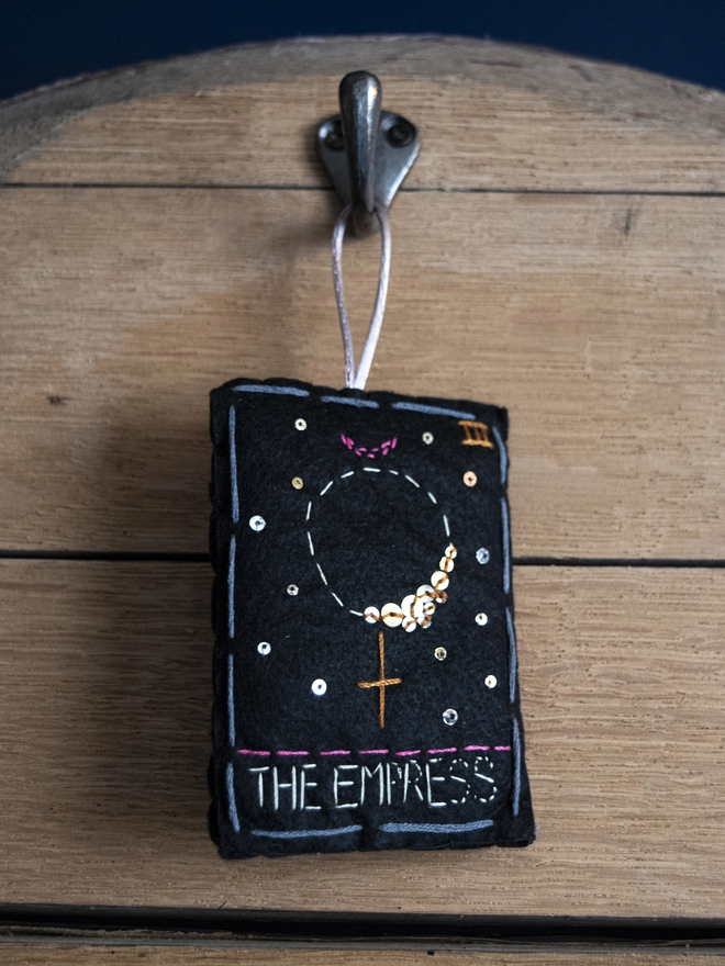 A handcrafted felt ornament with sequins and embroidery depicting "The Empress" tarot card. 