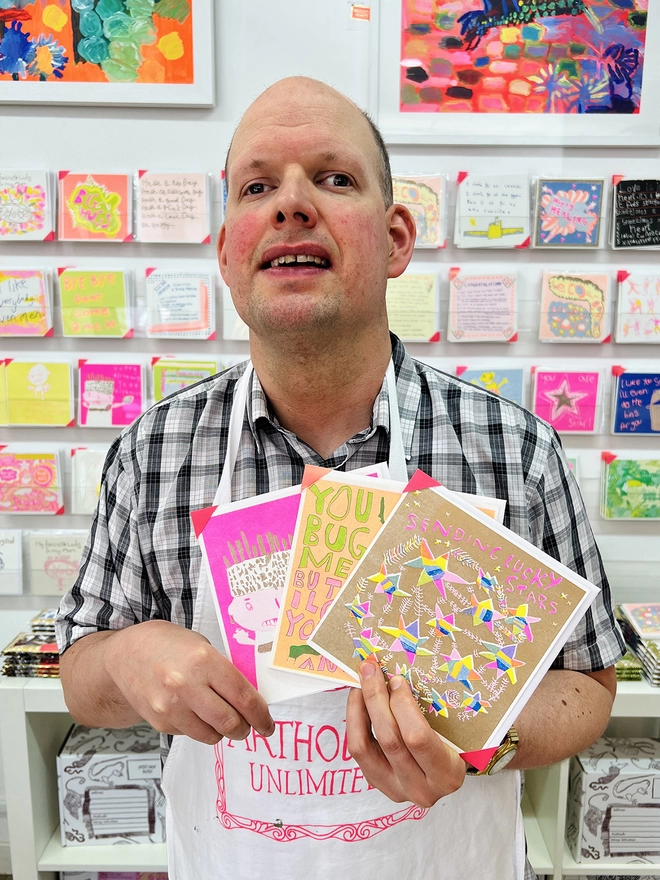 Artist holding a good luck card with coloured stars  on gold with the words Sending Lucky Stars