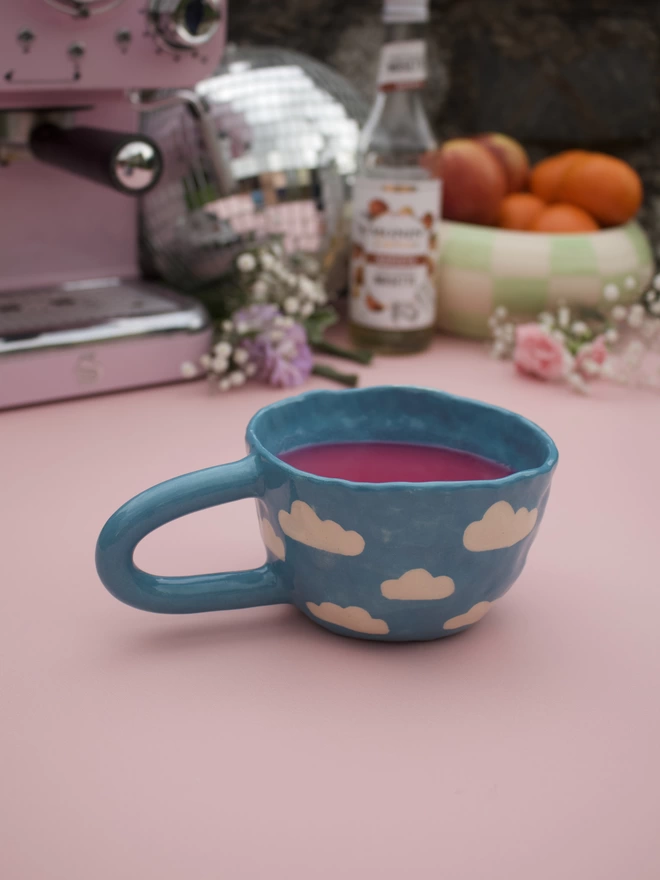 bright blue handmade stoneware pottery mug with white cloud pattern with pink liquid inside