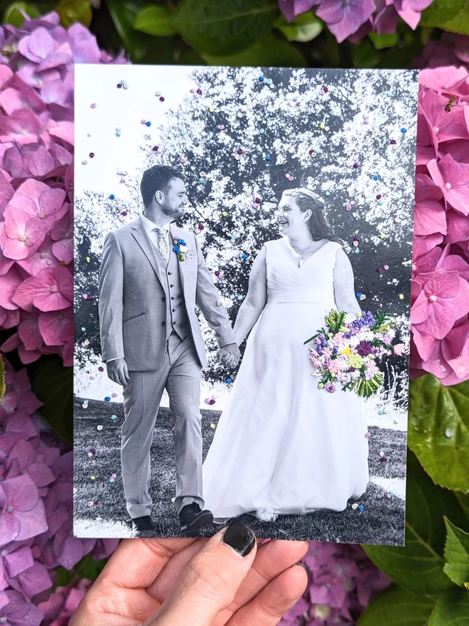 Wedding photograph with embroidered floral bouquet and confetti held against purple flowers