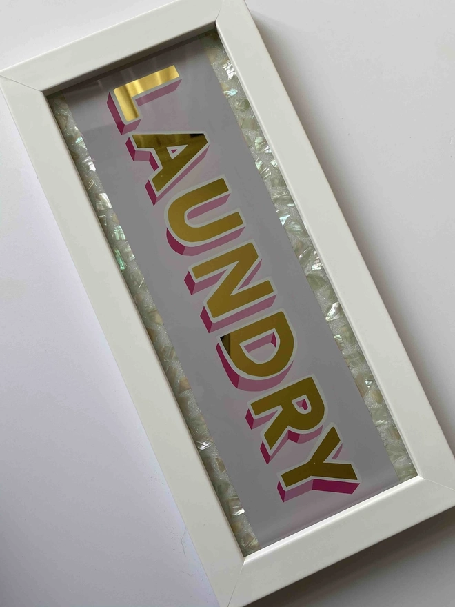 'Laundry' Glass And Gold Leaf Sign, a gold and glass sign sitting on a plain surface in a white frame. 