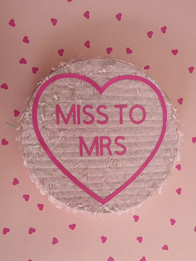hen do pinata in the shape of a love heart with the message miss to mrs in pink surrounded by heart shaped confetti